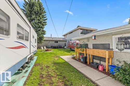 Expansive grassy yard featuring a concrete pathway, raised garden beds, and a fire pit area - 4622 Ada Boulevard, Edmonton, AB 