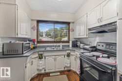 Functional kitchen featuring white cabinetry, dark countertops, a double basin sink beneath a window, and wood-finish flooring - 