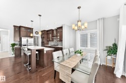 Open-concept living space featuring wood-finish flooring, a kitchen island with seating, dark wood cabinetry, stainless steel appliances, and a dining area with a window - 