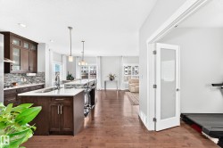 Modern kitchen featuring dark wood cabinetry, white countertops, a mosaic tile backsplash, and a large island with pendant lighting - 