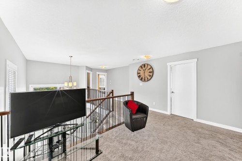 Carpeted loft area featuring a white door, light grey walls, and a wood-finish railing with black spindles - 3672 Claxton Place, Edmonton, AB 