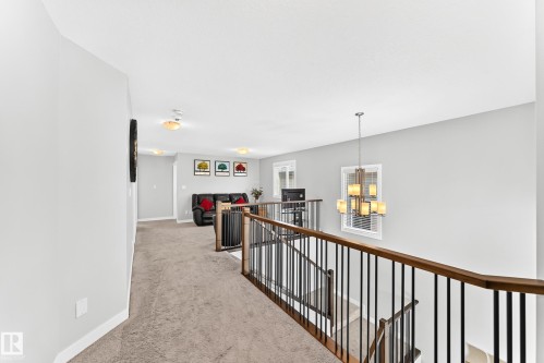Upper level landing featuring carpeted flooring, wood-finish handrails with black balusters, and a contemporary chandelier - 3672 Claxton Place, Edmonton, AB 