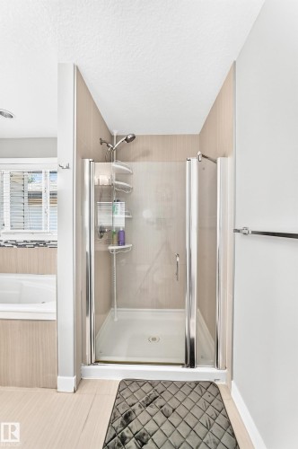 Glass-enclosed shower with a handheld showerhead and built-in shelving, complemented by a soaking tub with tile surround and a privacy window with blinds - 3672 Claxton Place, Edmonton, AB 