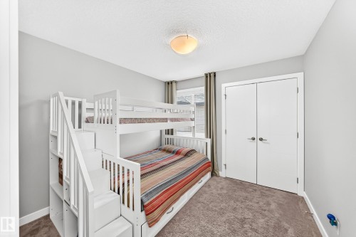 Room featuring light gray walls, textured carpet flooring, a flush-mount ceiling light, and white bi-fold closet doors with brushed nickel hardware - 3672 Claxton Place, Edmonton, AB 