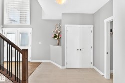 Foyer featuring light plank flooring, a dark wood-finish staircase with black spindles, a double-door entry with frosted glass, white trim, and a high window with blinds - 