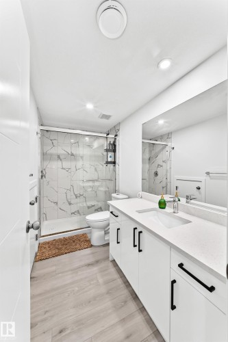Bathroom featuring a dual vanity with white cabinetry and dark hardware, set against light wood-finish flooring - 3672 Claxton Place, Edmonton, AB 