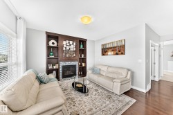 Living area featuring a built-in dark wood entertainment unit with shelving, a fireplace with a stone tile surround, and hardwood flooring - 