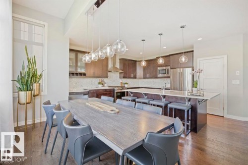 Open-concept kitchen and dining area featuring dark wood-finish flooring, a large island with seating, stainless steel appliances, and pendant lighting fixtures - 1004 Huckell Pl Sw, Edmonton, AB - Indoor Photo Showing Dining Room