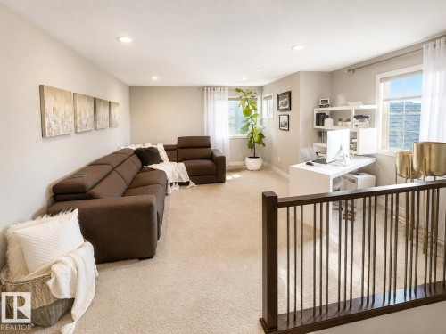Versatile bonus room featuring light-toned carpeting, ample natural light from multiple windows, recessed lighting, and a dark wood and metal baluster railing - 1004 Huckell Pl Sw, Edmonton, AB - Indoor