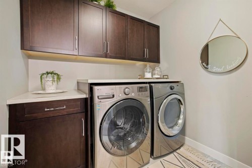 Laundry area featuring stacked front-load machines, dark wood-finish cabinetry with brushed nickel hardware, and light-toned countertops - 1004 Huckell Pl Sw, Edmonton, AB - Indoor Photo Showing Laundry Room
