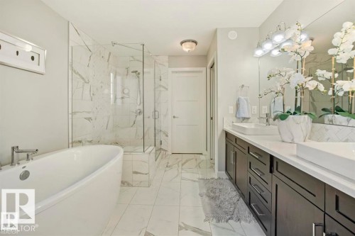 Modern bathroom featuring a freestanding soaking tub, a frameless glass shower enclosure with marble-look tile, a dual vanity with rectangular vessel sinks, dark wood-finish cabinetry, and a large wall-mounted mirror with overhead lighting - 1004 Huckell Pl Sw, Edmonton, AB - Indoor Photo Showing Bathroom