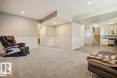Spacious lower level featuring plush carpeting, elegant wainscoting, recessed lighting, and a built-in wet bar with white cabinetry and stainless steel appliances - 1004 Huckell Pl Sw, Edmonton, AB - Indoor