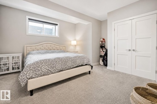 Light gray carpeting throughout a room featuring a window with white trim, light gray walls, and white bi-fold closet doors with modern hardware - 1004 Huckell Pl Sw, Edmonton, AB - Indoor Photo Showing Bedroom
