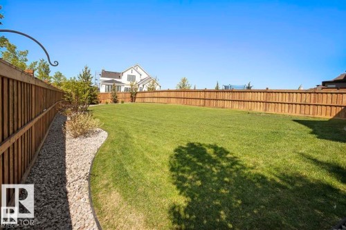 Expansive backyard featuring a manicured lawn, established privacy fencing, and a decorative gravel border with plantings - 1004 Huckell Pl Sw, Edmonton, AB - Outdoor