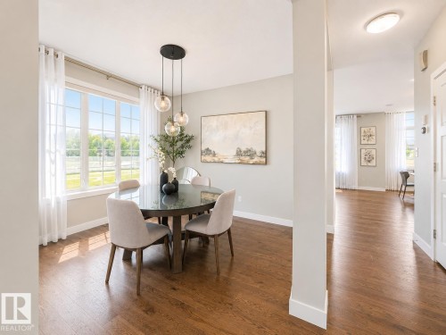 Dining area featuring a large window, dark wood-finish flooring, a modern pendant light fixture, light gray wall paint, and white trim - 1004 Huckell Pl Sw, Edmonton, AB - Indoor Photo Showing Dining Room