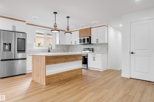 Kitchen featuring an island with wood-finish and white paneling, stone countertops, stainless steel appliances, and wood-finish flooring - 5512 150 Avenue, Edmonton, AB 