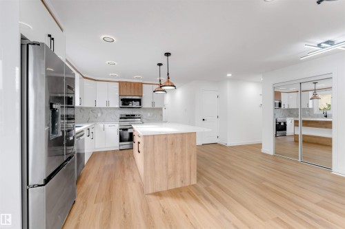 Contemporary kitchen featuring a white countertop island with wood-finish paneling, stainless steel appliances, white cabinetry with black pulls, and wood-finish flooring - 5512 150 Avenue, Edmonton, AB 