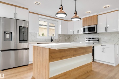 Contemporary kitchen featuring white cabinetry, wood-finish flooring, a central island with integrated shelving, stainless steel appliances, and pendant lighting - 5512 150 Avenue, Edmonton, AB 