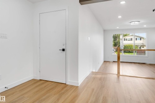 Bright interior entry featuring light wood-finish flooring, white walls, and a white door with matte black hardware - 5512 150 Avenue, Edmonton, AB 