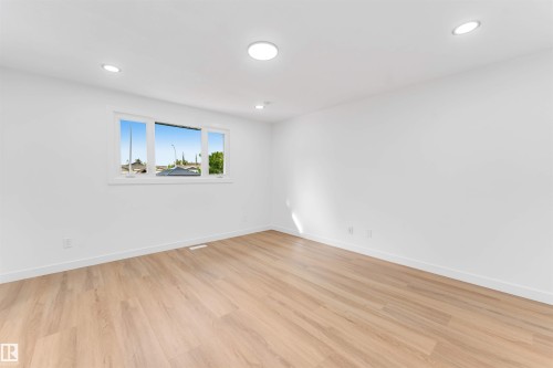 Spacious room featuring light wood-finish flooring, recessed lighting, and a multi-pane window with white trim - 5512 150 Avenue, Edmonton, AB 