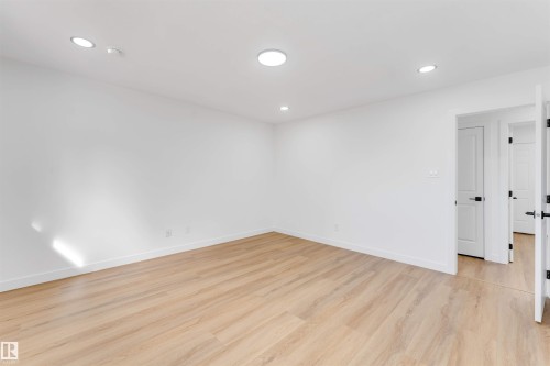 Bright interior space featuring light wood-finish flooring, recessed lighting, white baseboards, and white doors with matte black hardware - 5512 150 Avenue, Edmonton, AB 