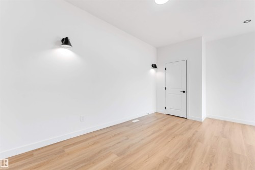 Spacious room featuring light wood-finish flooring, white walls, and contemporary black sconce lighting - 5512 150 Avenue, Edmonton, AB 