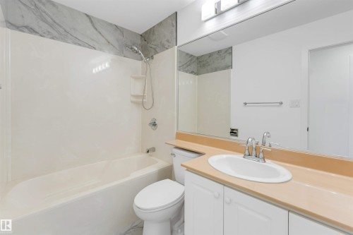 Bathroom featuring a white bathtub with a shower kit, a vanity with a drop-in sink, and an integrated countertop - 5512 150 Avenue, Edmonton, AB 