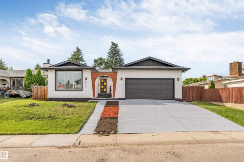Mid-century inspired exterior featuring white vertical siding with dark trim, a prominent arched entry, a dark panel garage door, and a concrete driveway - 5512 150 Avenue, Edmonton, AB 