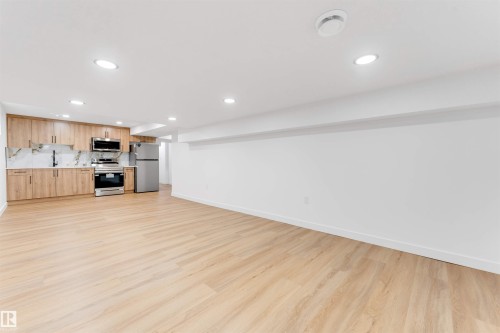 Open-concept living space featuring wood-finish flooring, recessed lighting, and a kitchen with stainless steel appliances, light wood cabinetry, and a patterned backsplash - 5512 150 Avenue, Edmonton, AB 