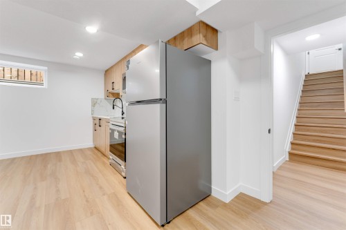 Compact kitchen area featuring wood-finish cabinetry, a stainless steel refrigerator, and a white marble-patterned backsplash - 5512 150 Avenue, Edmonton, AB 