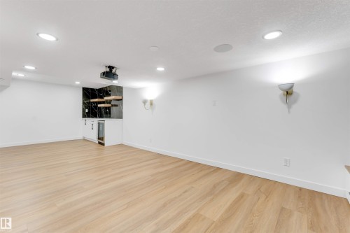 Spacious room featuring wood-finish flooring, recessed lighting, and a built-in wet bar with a dark stone-look backsplash and floating wood shelves - 5512 150 Avenue, Edmonton, AB 