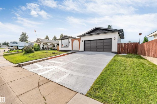 Exterior featuring white horizontal siding, a dark paneled garage door, a concrete driveway, a wooden fence, and a green lawn - 5512 150 Avenue, Edmonton, AB 
