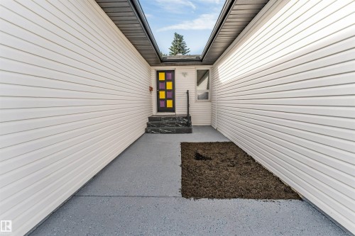 Covered entryway featuring light-toned horizontal siding, a dark framed door with colorful paneled inserts, and dark patterned steps - 5512 150 Avenue, Edmonton, AB 