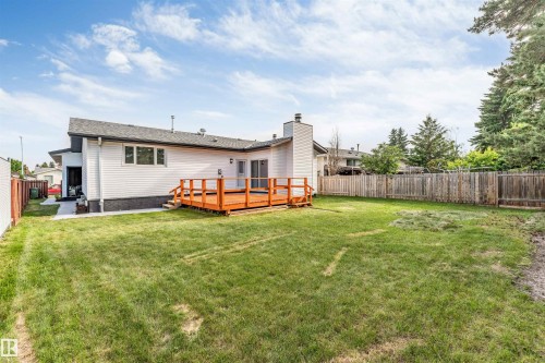 Expansive grass lawn with a wood deck, wood privacy fence, and concrete pathway - 5512 150 Avenue, Edmonton, AB 