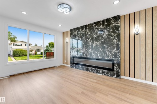 Spacious room featuring light wood-finish flooring, a large multi-pane window, and a contemporary linear fireplace - 5512 150 Avenue, Edmonton, AB 