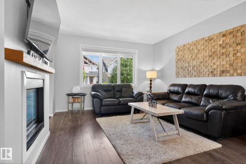 Living area featuring wood-finish flooring, a white trim window, a built-in fireplace with a wooden mantel, and light-toned walls - 3456 Cutler Crescent, Edmonton, AB - Indoor Photo Showing Living Room With Fireplace