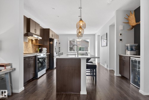 Open-concept kitchen featuring dark wood cabinetry, stainless steel appliances, a center island with seating, pendant lighting, and wood-finish flooring - 3456 Cutler Crescent, Edmonton, AB - Indoor Photo Showing Kitchen