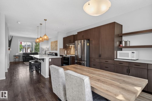 Open-concept kitchen and living area featuring wood-finish flooring, dark wood cabinetry, a central island with countertop seating, stainless steel appliances, and a built-in microwave shelf - 3456 Cutler Crescent, Edmonton, AB - Indoor Photo Showing Kitchen With Upgraded Kitchen