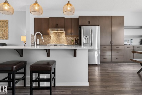 Gourmet kitchen featuring a peninsula with seating, stainless steel appliances, dark wood cabinetry, a tile backsplash, and three pendant lights - 3456 Cutler Crescent, Edmonton, AB - Indoor Photo Showing Kitchen With Upgraded Kitchen