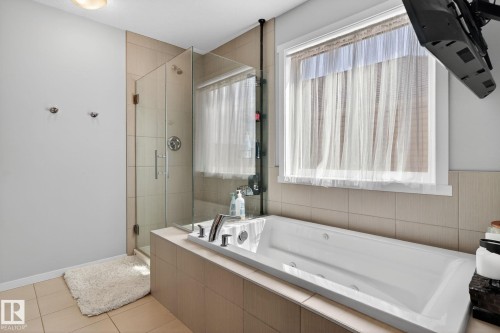 Bathroom featuring a built-in soaking tub, glass-enclosed shower, wall-mounted shower fixtures, and light-toned tile flooring - 3456 Cutler Crescent, Edmonton, AB - Indoor Photo Showing Bathroom