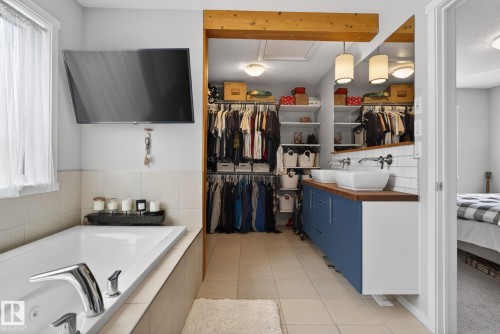 Spa-inspired bathroom featuring a built-in soaking tub with chrome fixtures, a dual vessel sink vanity with a wood-finish countertop and blue cabinetry, and an expansive walk-in closet with custom shelving and hanging storage - 3456 Cutler Crescent, Edmonton, AB - Indoor Photo Showing Bathroom