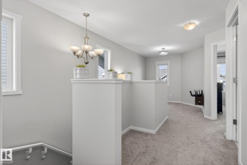 Open upper-level landing featuring light gray walls, plush gray carpeting, white trim, and a brushed nickel chandelier - 3456 Cutler Crescent, Edmonton, AB - Indoor Photo Showing Other Room