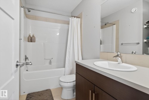 Bathroom featuring a white integrated bathtub and shower, a dark wood-finish vanity with a light countertop, an oval undermount sink, and a large mirror - 3456 Cutler Crescent, Edmonton, AB - Indoor Photo Showing Bathroom