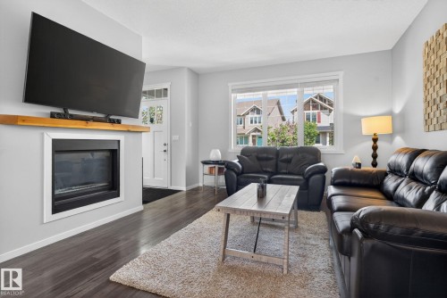 Living area featuring an integrated fireplace with a wood-finish mantle, large window, and dark wood-finish flooring - 3456 Cutler Crescent, Edmonton, AB - Indoor Photo Showing Living Room With Fireplace