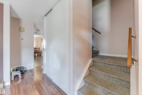 Entryway featuring wood-finish flooring, a full-height sliding closet, and a carpeted staircase with a wood handrail - 24 1651 46 Street, Edmonton, AB 
