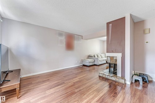 Living area featuring wood-finish flooring, a stone-faced fireplace with a hearth, and a textured white ceiling - 24 1651 46 Street, Edmonton, AB 