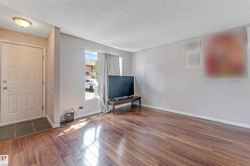 Living area featuring wood-finish flooring, neutral wall tones, a front entry door with panel detailing, and a window with natural light - 24 1651 46 Street, Edmonton, AB 