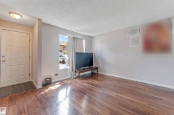 Living area featuring wood-finish flooring, neutral wall tones, a front entry door with panel detailing, and a window with natural light - 