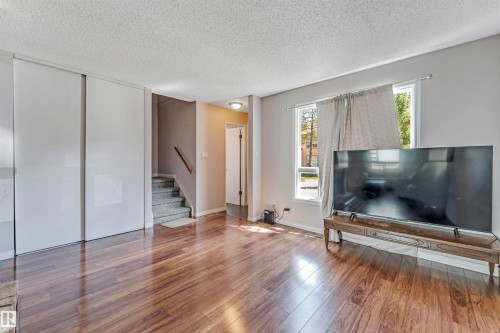 Spacious room featuring rich wood-finish flooring, light-toned walls, and multiple windows - 24 1651 46 Street, Edmonton, AB 