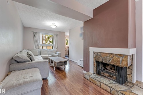 Living area featuring wood-finish flooring, a stone-clad fireplace with hearth, and a window with natural light - 24 1651 46 Street, Edmonton, AB 
